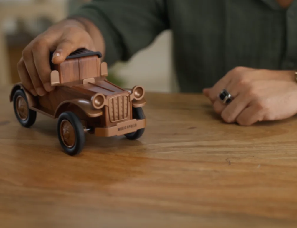 Hands pushing a wooden toy car across a wooden table
